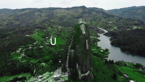 A Large Rock In The Middle Of A Lush Green Valley With The Letter U Above It GIF