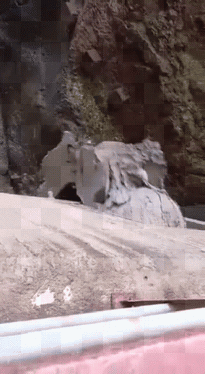 A Large Rock Is Sitting On The Side Of A Road Next To A Waterfall . GIF