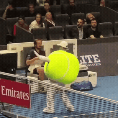 A Large Tennis Ball Is Being Thrown On A Tennis Court With A Sign That Says Emirates On It GIF