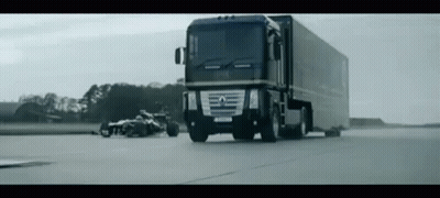A Large Truck Is Driving Down A Road Next To A Race Car On The Side Of The Road . GIF