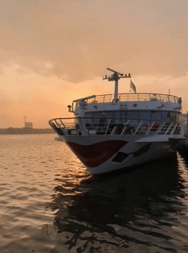 A Large White And Red Boat Is Docked In The Water At Sunset GIF