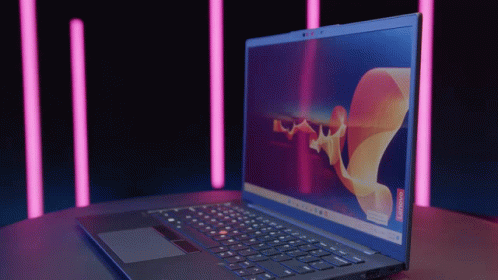 A Lenovo Laptop Is Open On A Table With Pink Lights In The Background GIF
