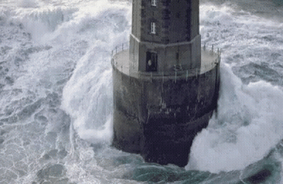 A Lighthouse In The Middle Of The Ocean With Waves Crashing Against It GIF