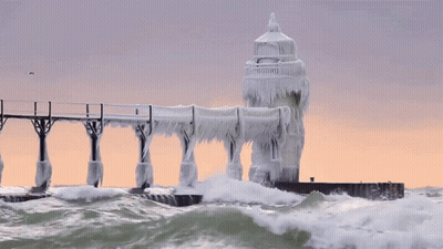 A Lighthouse Is Covered In Ice And Waves Crashing Against It GIF