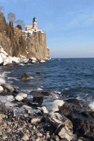 A Lighthouse Sits On Top Of A Rocky Cliff Overlooking The Ocean GIF