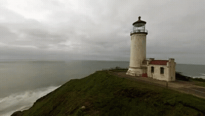 A Lighthouse Sitting On Top Of A Hill Overlooking The Ocean GIF