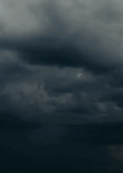 A Lightning Bolt Strikes In A Dark Cloudy Sky . GIF