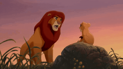 A Lion And A Cub Are Standing On A Rock In The Grass GIF