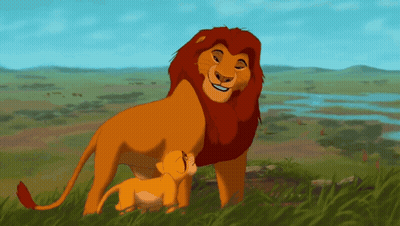 A Lion And A Cub Standing In The Grass GIF