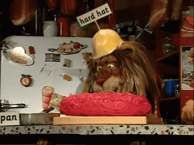 A Lion Wearing A Hard Hat Is Sitting On A Cutting Board GIF