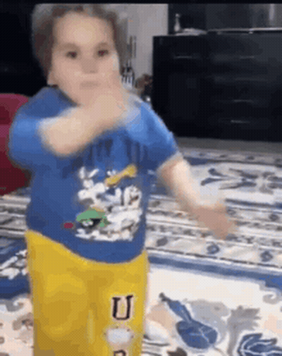 A Little Boy In A Blue Shirt And Yellow Pants Is Dancing On A Rug . GIF