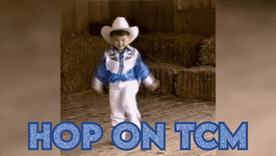 A Little Boy In A Cowboy Outfit Is Dancing In Front Of Hay Bales GIF