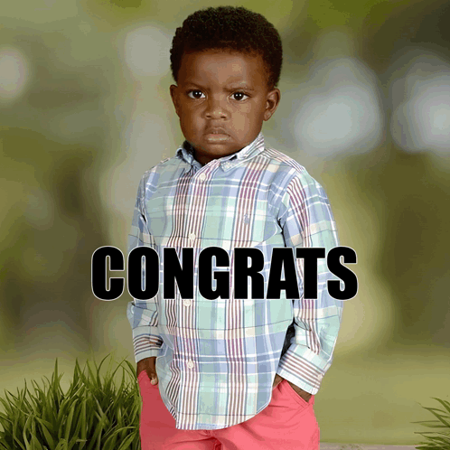 A Little Boy In A Plaid Shirt Is Standing In Front Of A Sign That Says Congrats GIF