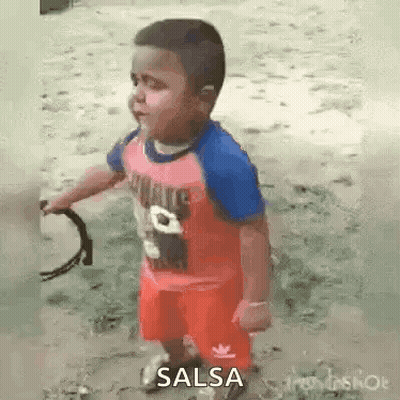 A Little Boy In A Red Shirt And Red Shorts Is Holding A Tambourine In His Hands . GIF