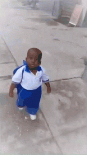 A Little Boy In A White Shirt And Blue Pants Is Walking Down A Sidewalk GIF