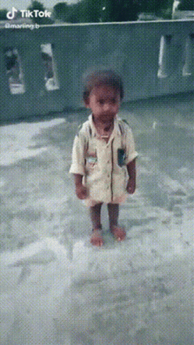 A Little Boy In A Yellow Shirt Is Standing In A Puddle Of Water GIF