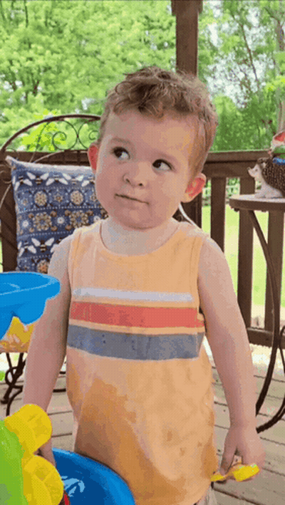 A Little Boy In An Orange Tank Top Is Standing On A Porch Looking Up GIF