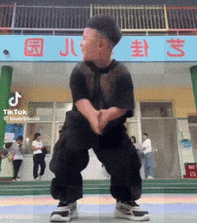 A Little Boy Is Dancing In Front Of A Building That Says Tiktok GIF