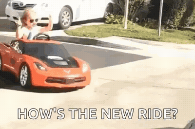 A Little Boy Is Driving A Red Toy Car Down The Street . GIF