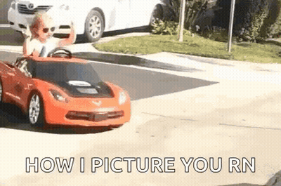 A Little Boy Is Driving A Red Toy Car On A Street . GIF
