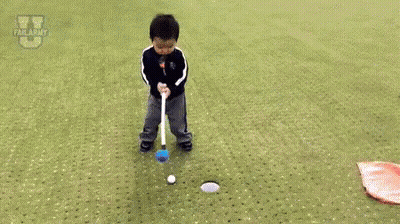 A Little Boy Is Laying On The Ground On A Golf Course Next To A Flag And A Golf Club . GIF