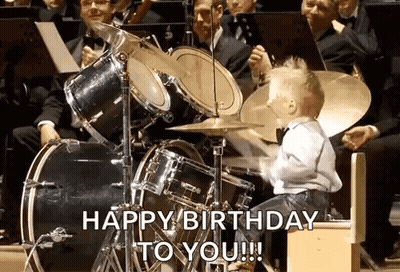 A Little Boy Is Playing Drums In Front Of An Orchestra And Says Happy Birthday To You ! GIF