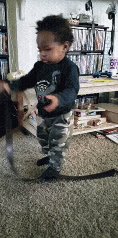 A Little Boy Is Playing With A Remote Control In Front Of A Sign That Says " Make It " GIF