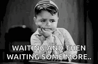 A Little Boy Is Sitting At A Desk With His Hand On His Chin And The Words `` Waiting And Then Waiting Some More '' . GIF
