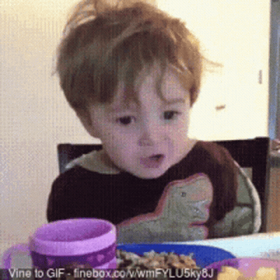 A Little Boy Is Sitting At A Table With A Plate Of Food And A Pink Cup GIF