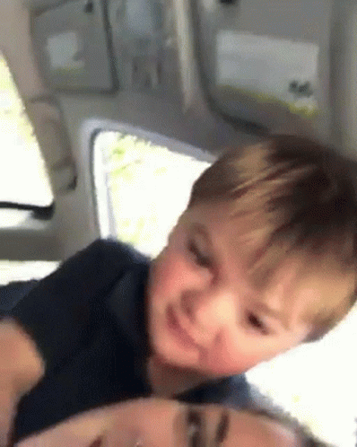 A Little Boy Is Sitting On The Back Of A Woman In A Car . GIF