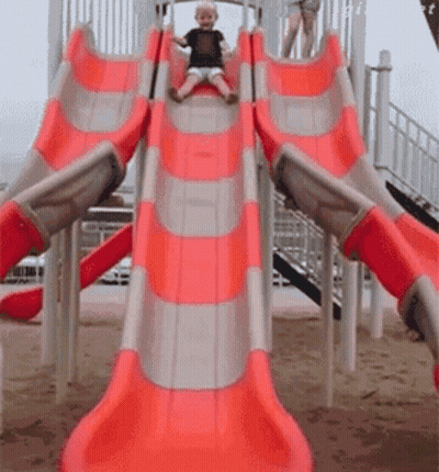 A Little Boy Is Sliding Down A Red And Gray Slide GIF