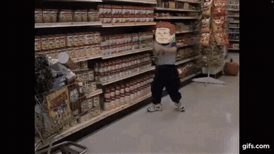 A Little Boy Is Standing In A Grocery Store Holding A Bottle Of Tomato Sauce . GIF