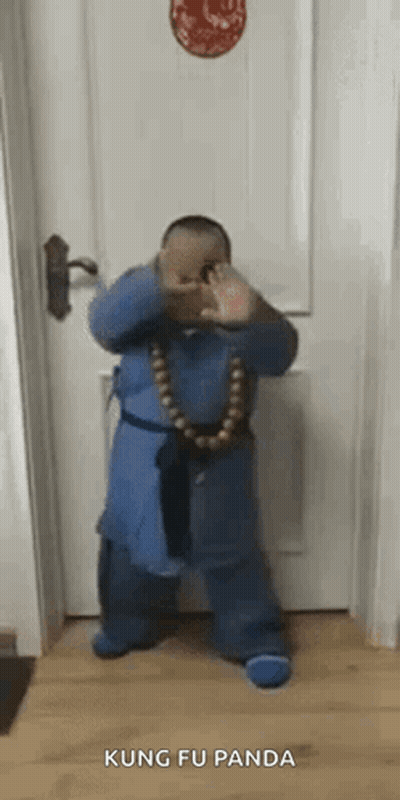 A Little Boy Is Standing In Front Of A Door Wearing A Blue Robe And A Necklace Of Beads . GIF