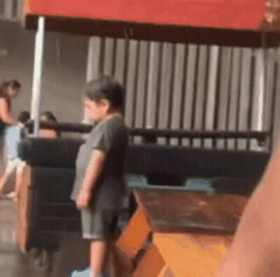 A Little Boy Is Standing In Front Of A Red Canopy . GIF