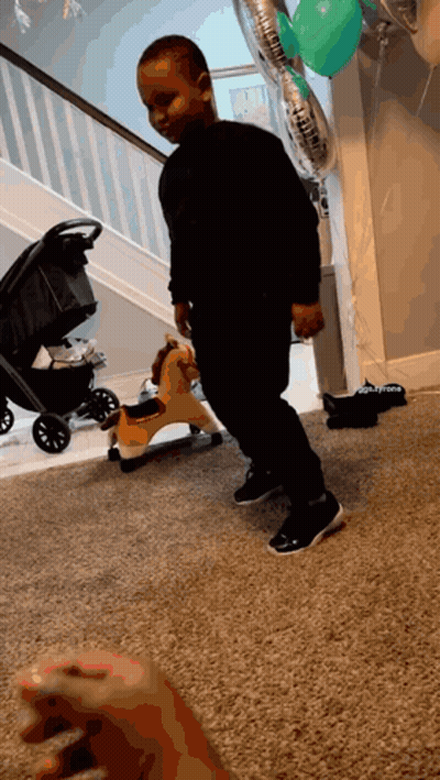 A Little Boy Is Standing In Front Of A Rocking Horse And Balloons That Say ' Daddy ' On Them GIF