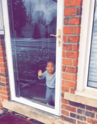 A Little Boy Is Standing In Front Of A Sliding Glass Door And Giving The Middle Finger . GIF