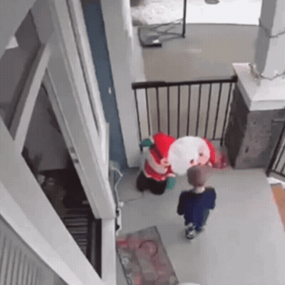 A Little Boy Is Standing Next To A Stuffed Santa Claus In A House . GIF