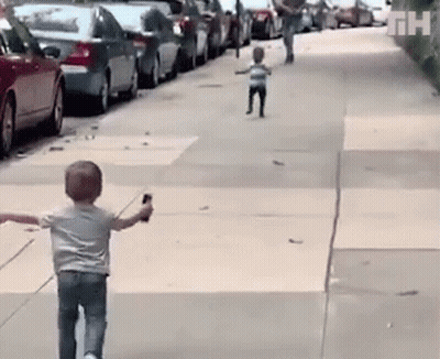 A Little Boy Is Walking Down A Sidewalk While Holding A Cell Phone In His Hand . GIF