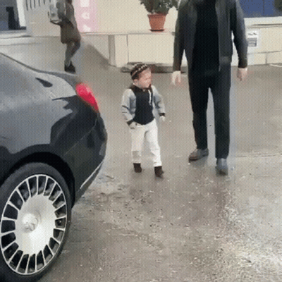 A Little Boy Is Walking Next To A Man In A Black Jacket . GIF