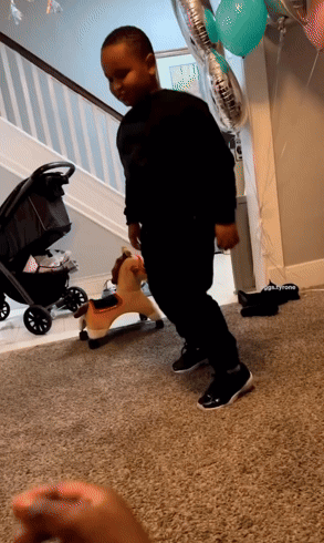 A Little Boy Stands In Front Of A Rocking Horse And Balloons That Say ' Daddy ' On Them GIF