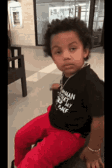 A Little Boy Wearing A Black Shirt And Red Pants Is Sitting In A Chair . GIF