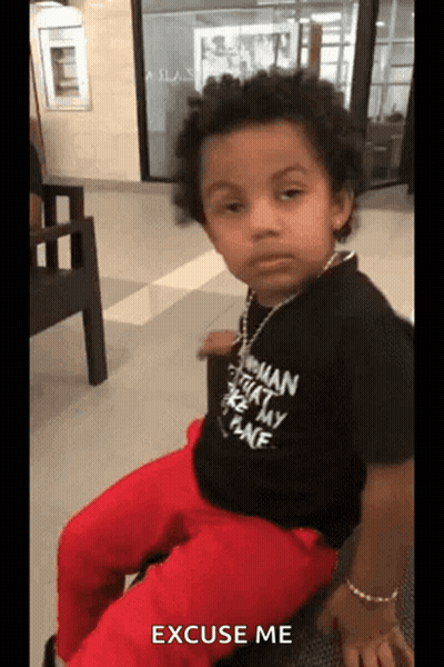 A Little Boy Wearing A Black Shirt That Says Excuse Me Is Sitting On A Chair GIF