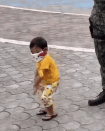 A Little Boy Wearing A Face Mask Is Standing On A Brick Sidewalk . GIF