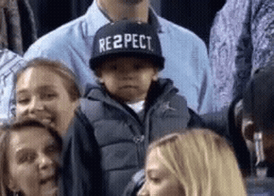 A Little Boy Wearing A Hat That Says Respect Is Sitting In The Stands . GIF