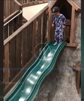 A Little Boy Wearing A Hat With The Letter P On It Stands On A Slide GIF
