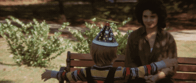 A Little Boy Wearing A Party Hat Sits On A Bench GIF