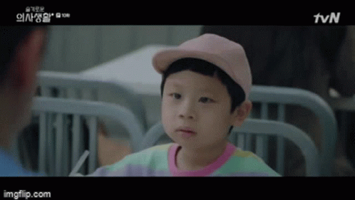 A Little Boy Wearing A Pink Hat And A Colorful Shirt Is Sitting In A Hospital Bed . GIF