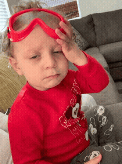 A Little Boy Wearing A Red Shirt With Mickey Mouse On It Is Rubbing His Forehead GIF