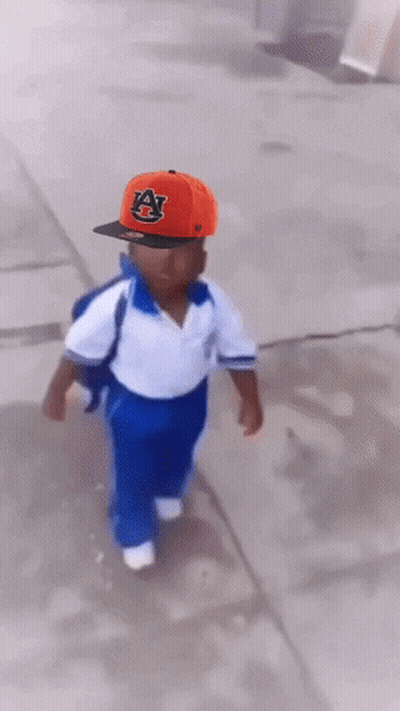 A Little Boy Wearing An Auburn Hat Is Running Down The Street GIF