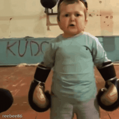 A Little Boy Wearing Boxing Gloves Is Standing In Front Of A Wall That Says Kudc GIF